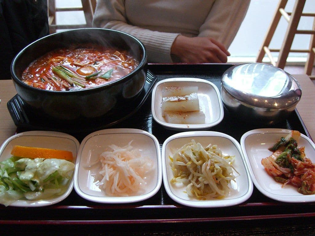 A Korean meal tray with a bubbling stew surrounded by free side dishes
